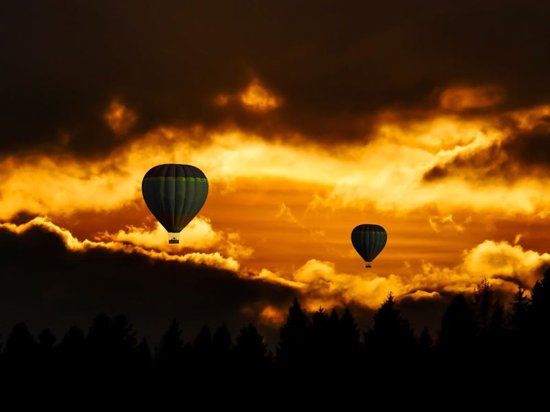hot air balloons float against a stunning sunset sky with dramatic clo image