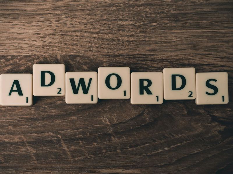 scrabble tiles spelling 'adwords' on a wooden surface, symbolizing dig image